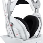 Auriculares gaming blancos Logitech Astro A50 sobre su base de carga inalámbrica junto a mandos de consola