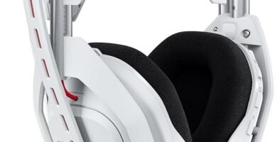Auriculares gaming blancos Logitech Astro A50 sobre su base de carga inalámbrica junto a mandos de consola